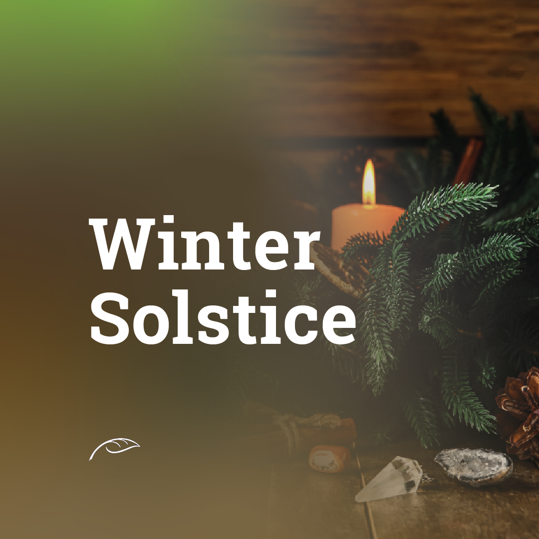 White text reading “Winter Solstice” appears over a dark, warm-toned background. A lit candle is surrounded by evergreen branches on a wooden surface, with a pine cone, crystals, and small decorative items in the foreground.